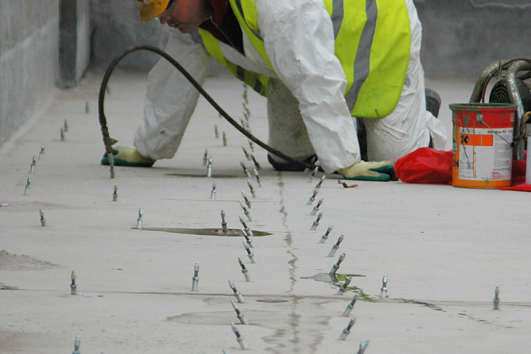 Person injecting polyurethane under a large concrete floor slab.
