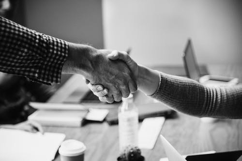 Black and white image of two people shaking hands over a desk.